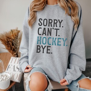 May include: Gray sweatshirt with the text "Sorry. Can't. Hockey. Bye." in black and blue lettering.