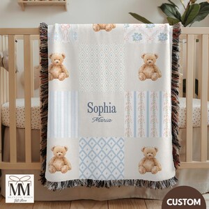 Peut inclure: Une couverture patchwork beige et bleue pour bébé avec un motif d'ours en peluche. La couverture porte le nom "Sophia Maria" en écriture cursive. La couverture est frangée sur les bords et est présentée sur un berceau.