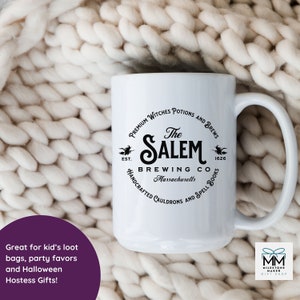 Puede incluir: Taza de cer&aacute;mica blanca con un gr&aacute;fico negro de un caldero de bruja y el texto "The Salem Brewing Co. Massachusetts" con una bruja volando en una escoba a cada lado del texto. El texto "Premium Witches Potions and Brews" est&aacute; por encima del gr&aacute;fico y "Handcrafted Cauldrons and Spell Books" est&aacute; por debajo del gr&aacute;fico.
