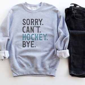 May include: Gray sweatshirt with the text "SORRY. CAN'T. HOCKEY. BYE." in black and blue lettering.