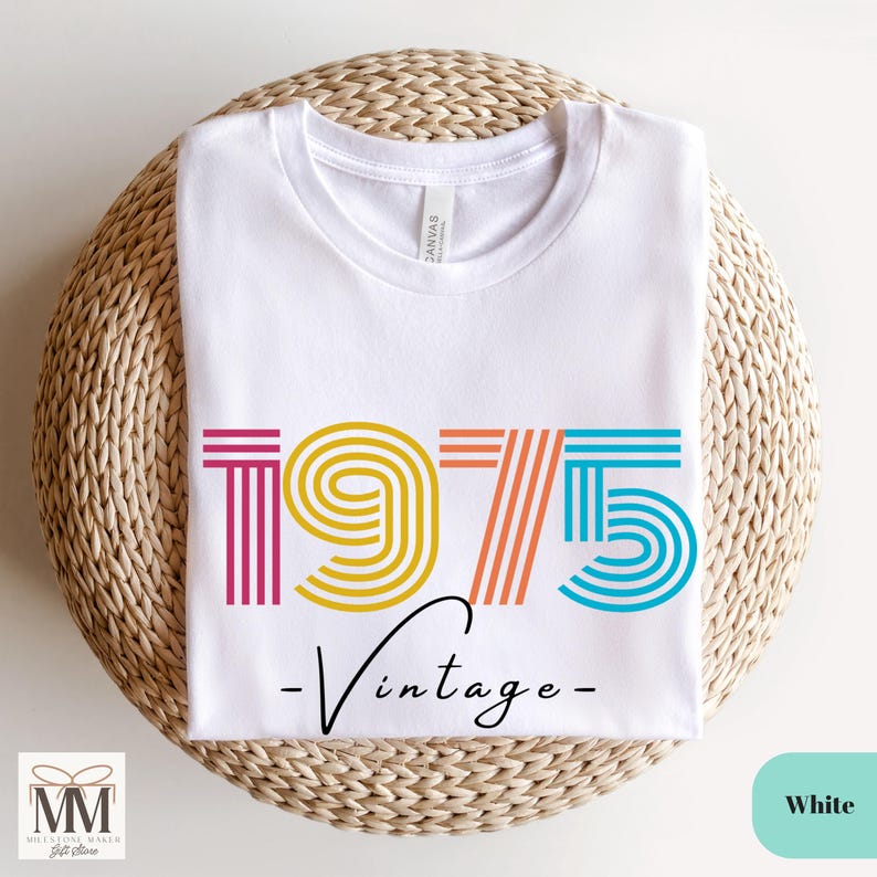 以下が含まれることがあります： 白いTシャツに、カラフルな1975年のグラフィックと「ヴィンテージ」という文字がプリントされています。