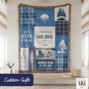 Peut inclure: Une couverture tissée bleue et blanche avec un motif patchwork. La couverture présente des graphiques sur le thème du lac, notamment des arbres, un coucher de soleil et le texte "Life is Better at the Lake" et "Lake House". Le texte "Custom Gift" est également visible.