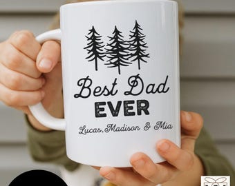May include: White ceramic mug with the text "Best Dad Ever" in black script and block letters, along with the names "Lucas, Madison & Mia". The mug also features a graphic of three pine trees.