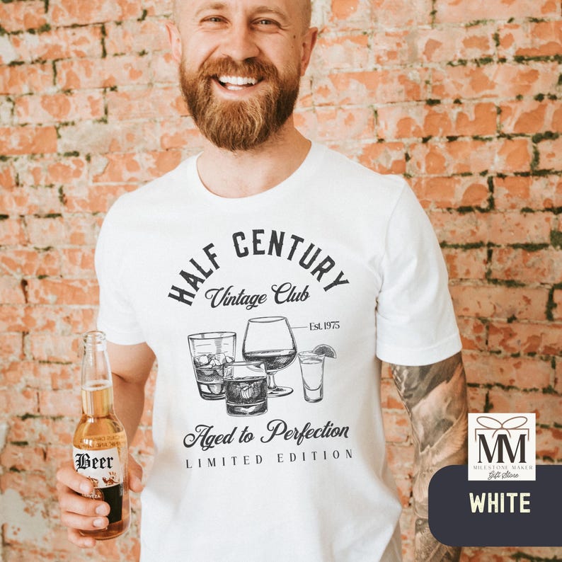 May include: White t-shirt with a graphic design featuring the text "HALF CENTURY Vintage Club" and "Aged to Perfection". The design includes illustrations of various glasses. A beer bottle is held in the hand.