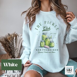 Puede incluir: Sudadera blanca con un gr&aacute;fico verde de tarros de pepinillos y el texto "THE PICKLE Club SAN FRANCISCO Gourmet Pickles and Brines". La sudadera tiene cuello redondo y mangas largas.