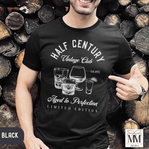 May include: Black t-shirt with white text and illustrations. The shirt features the words "HALF CENTURY Vintage Club" and "Aged to Perfection, Limited Edition." The design includes drawings of various glasses. The text "Est. 1975" is also present.