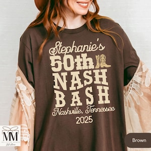 May include: Brown t-shirt with the text "Stephanie's 50th NASH BASH Nashville, Tennessee 2025" in beige lettering. The text is decorated with a pair of brown cowboy boots.