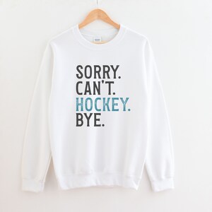 May include: White sweatshirt with the text "SORRY. CAN'T. HOCKEY. BYE." in black and blue.