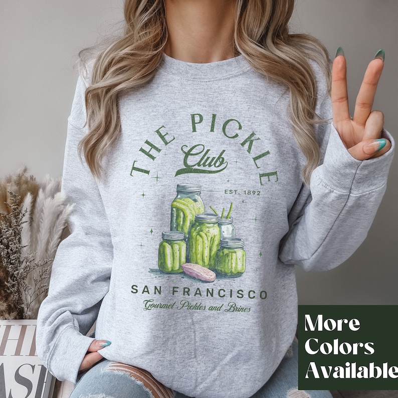 Puede incluir: Sudadera gris claro con un dise&ntilde;o verde que dice "THE PICKLE CLUB" sobre una ilustraci&oacute;n de frascos de pepinillos. Debajo del dise&ntilde;o, dice "SAN FRANCISCO Gourmet Pickles and Brines". Tambi&eacute;n se ve el texto "EST. 1892".