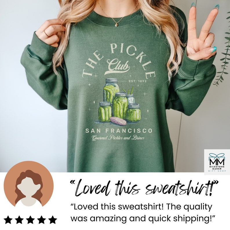 Puede incluir: Sudadera verde con un gr&aacute;fico de "The Pickle Club". El dise&ntilde;o presenta frascos de pepinillos y el texto "San Francisco Gourmet Pickles and Brines". La sudadera tiene cuello redondo y mangas largas.
