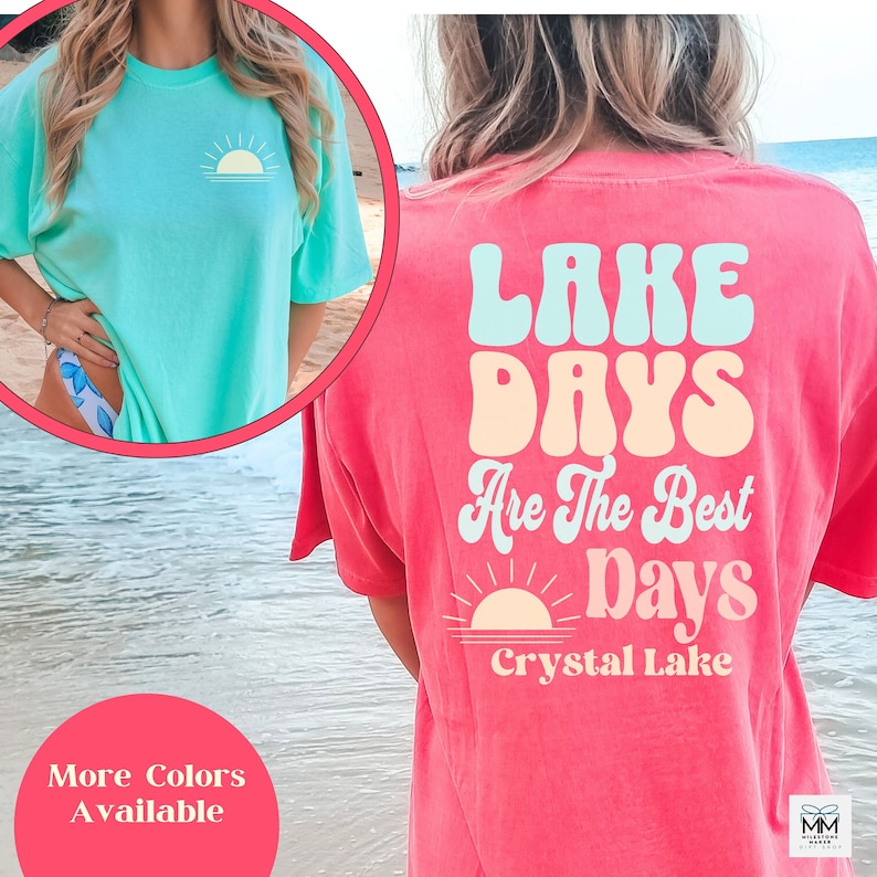 Może przedstawiać: Pokazano dwie koszulki. Jedna jest w kolorze jasnego turkusu z małą grafiką słońca z przodu. Druga jest w kolorze koralowym ze słowami "Lake Days Are The Best Days" i grafiką słońca z tyłu. Tekst "Crystal Lake" znajduje się r&oacute;wnież z tyłu.
