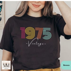 以下が含まれることがあります： カラフルな1975年のグラフィックと「ヴィンテージ」というテキストが書かれた黒いTシャツ。