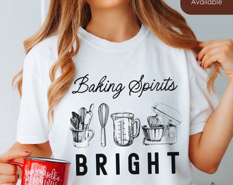 May include: White t-shirt with black text that reads "Baking Spirits Bright". The text is surrounded by a graphic of baking tools, including a whisk, measuring cup, and a stand mixer.
