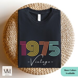 以下が含まれることがあります： 虹色のヴィンテージな1975年のデザインが施された黒いTシャツ。年の下に「ヴィンテージ」という文字が書かれています。
