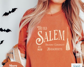 May include: A burnt orange t-shirt with a vintage-style graphic that reads "The Old Salem Broom Company Est. 1626 Massachusetts". The graphic features a stylized broom with a brown handle and straw bristles.
