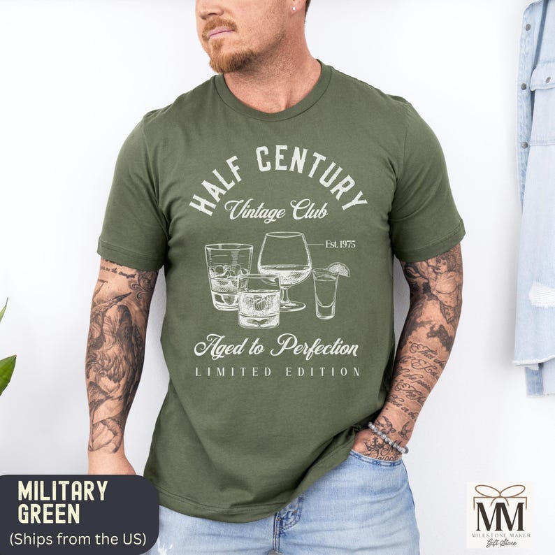May include: Military green t-shirt with a white graphic design featuring glassware and the text "HALF CENTURY Vintage Club, Aged to Perfection, Est. 1975, LIMITED EDITION". The shirt has a crew neck.