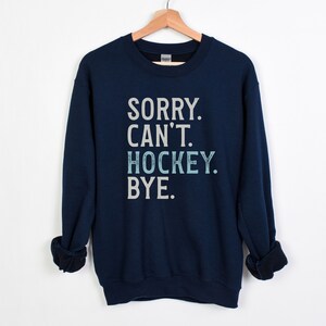 May include: Navy blue sweatshirt with the text "SORRY. CAN'T. HOCKEY. BYE." in white and light blue lettering.