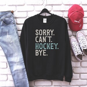 May include: Black sweatshirt with the text "SORRY. CAN'T. HOCKEY. BYE." in white and blue lettering.