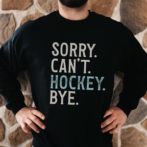 May include: Black sweatshirt with the text "SORRY. CAN'T. HOCKEY. BYE." in white with the word "HOCKEY" in light blue.