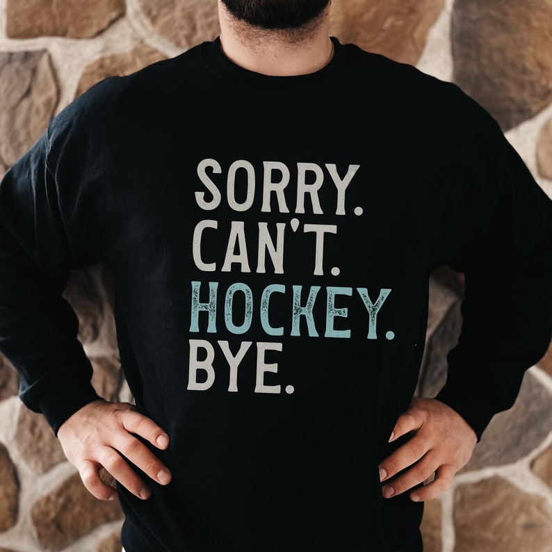 May include: Black sweatshirt with the text "SORRY. CAN'T. HOCKEY. BYE." in white with the word "HOCKEY" in light blue.