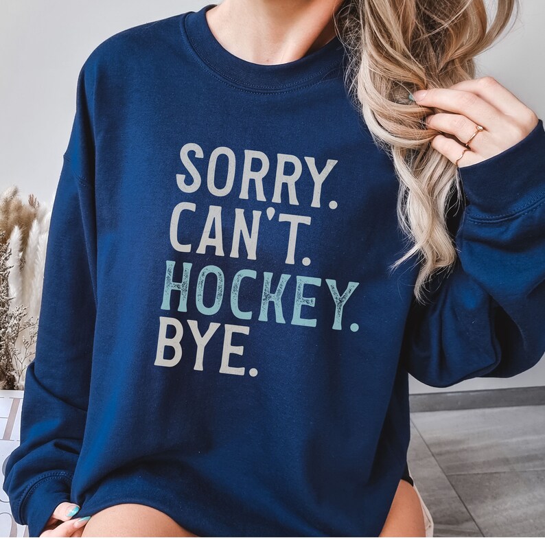 May include: A navy blue sweatshirt with the text "SORRY. CAN'T. HOCKEY. BYE." printed in white and light blue.