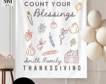 Op de afbeelding: Witte Thanksgiving-banner met de tekst "Count Your Blessings" en "Smith Family Thanksgiving". De banner bevat kleurrijke illustraties van verschillende groenten en fruit, waaronder een wortel, tomaat en peer.