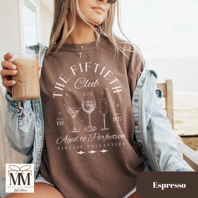 May include: Espresso-colored t-shirt with the text "The Fiftieth Club" and three wine glasses. The shirt also includes the text "Aged to Perfection" and "Vintage Collection". The shirt is a vintage style.