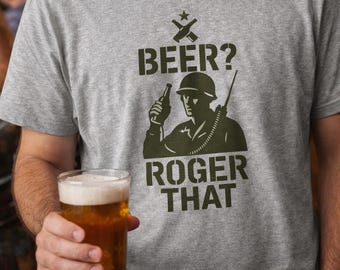 May include: A heather gray crew neck t-shirt featuring a dark green graphic of a soldier in a helmet holding a bottle. Above the soldier is the text BEER? and below is the text ROGER THAT, with a small star and crossed rifles icon above.