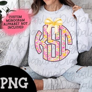 May include: A gray sweatshirt with a pink and yellow floral monogram design. The monogram is in a circle with a yellow bow on top. The text "CUSTOM MONOGRAM ALPHABET NOT INCLUDED" is on the sweatshirt.
