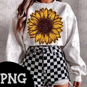 May include: White sweatshirt featuring a large sunflower graphic with yellow petals and a brown center. The sweatshirt is paired with black and white checkered shorts. The image has a PNG watermark in the bottom left corner.