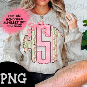 May include: A pink and green monogram design with a bow on a white sweatshirt. The monogram is in the shape of the letters "AS" with a floral pattern. The text "CUSTOM MONOGRAM ALPHABET NOT INCLUDED" is also visible.