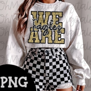 May include: White sweatshirt with the text "WE Eagles ARE" in gold and black. The sweatshirt is paired with black and white checkered shorts. The image has a PNG watermark in the bottom left corner.