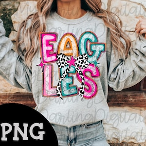 May include: A gray sweatshirt with the word "EAGLES" in colorful, bold letters. The letters are outlined in pink, teal, and orange, with a black and white bow in the center. Pink star accents are on either side.