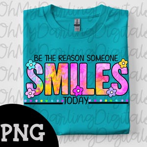 Könnte beinhalten: Ein gefaltetes, türkisfarbenes T-Shirt mit dem Aufdruck "BE THE REASON SOMEONE SMILES TODAY". Das Wort "SMILES" ist in großen, bunten Buchstaben mit Batik-Effekt und Blumendesign geschrieben.