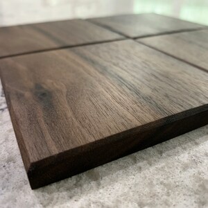 May include: Four square wooden coasters made of dark walnut wood. The coasters have a smooth, polished finish and a dark brown color.