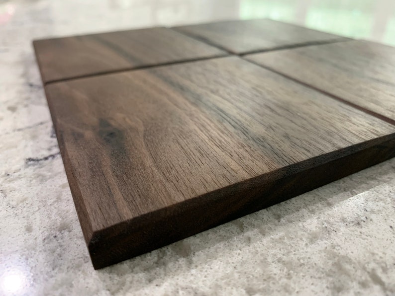 May include: Four square wooden coasters made of dark walnut wood. The coasters have a smooth, polished finish and a dark brown color.