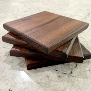 May include: Four square wooden coasters made of dark walnut wood. The coasters are stacked on top of each other.