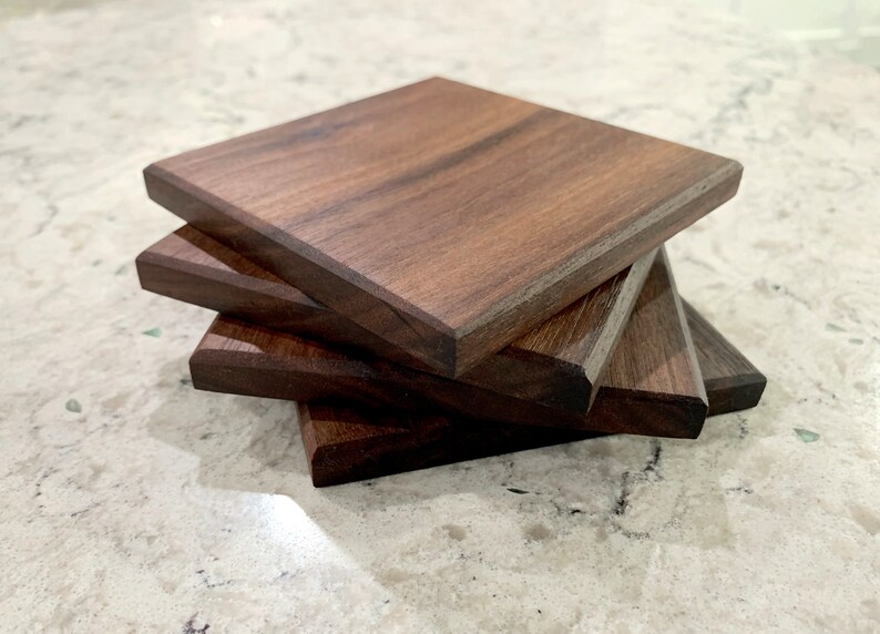 May include: Four square wooden coasters made of dark walnut wood. The coasters are stacked on top of each other.
