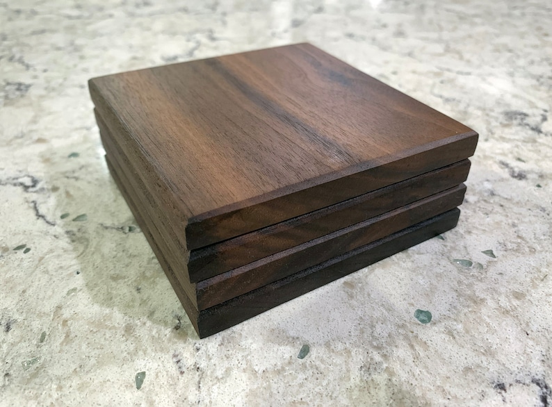 May include: A stack of four square wooden coasters made of dark brown walnut wood.