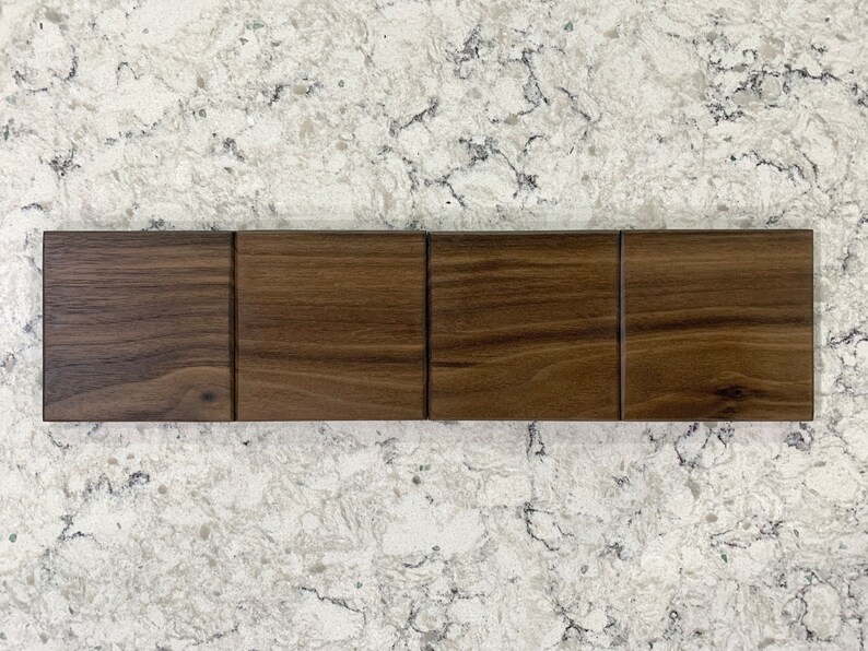 May include: Four wood samples in a row, each a different shade of brown. The wood has a natural grain pattern.