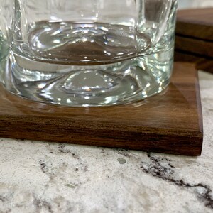 May include: A close-up of a clear glass on a dark brown wooden coaster. The coaster has a smooth, polished surface.
