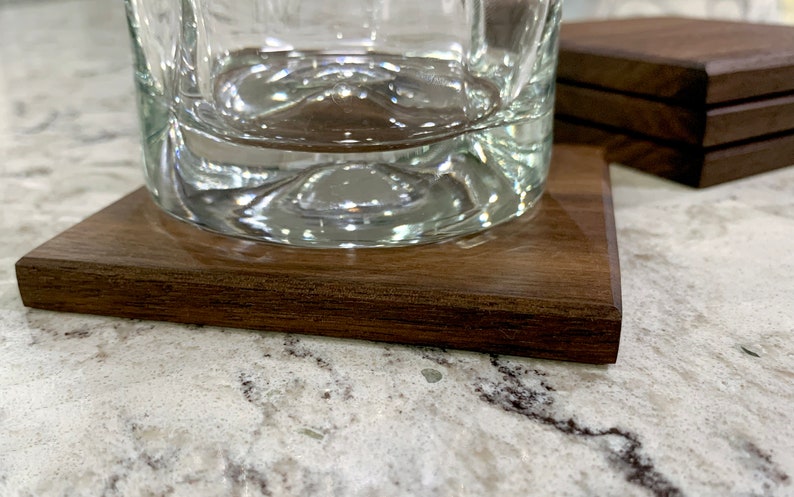 May include: A close-up of a clear glass on a dark brown wooden coaster. The coaster has a smooth, polished surface.