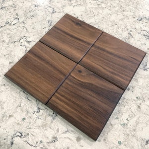 May include: Four square tiles made of dark brown wood with a wood grain pattern.