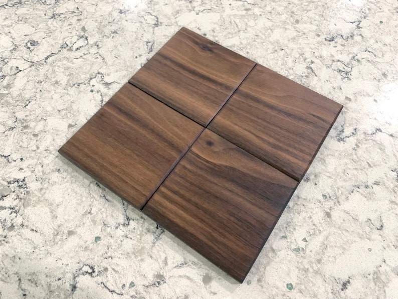 May include: Four square tiles made of dark brown wood with a wood grain pattern.