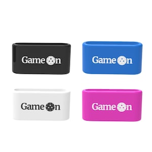 Op de afbeelding: Vier rechthoekige polsbandjes in zwart, blauw, wit en roze. Elke band heeft de woorden "Game on" in het wit gedrukt, met een pickleball-afbeelding die de "o" vervangt. De bandjes zijn gemaakt van flexibel materiaal.