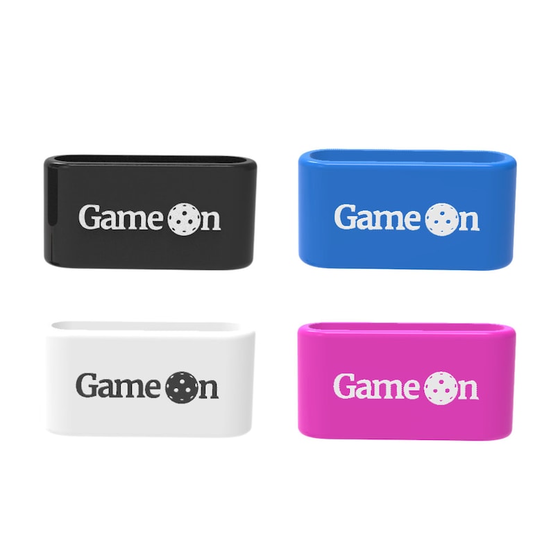 Op de afbeelding: Vier rechthoekige polsbandjes in zwart, blauw, wit en roze. Elke band heeft de woorden "Game on" in het wit gedrukt, met een pickleball-afbeelding die de "o" vervangt. De bandjes zijn gemaakt van flexibel materiaal.