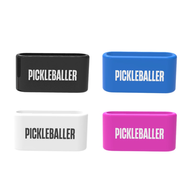 Op de afbeelding: Vier rechthoekige, open banden in zwart, blauw, wit en roze. Elke band heeft het woord "PICKLEBALLER" in witte letters. De banden zijn waarschijnlijk gemaakt van een glad, stevig materiaal.