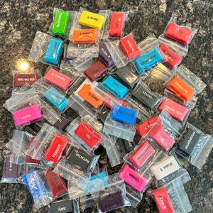 Puede incluir: Una colecci&oacute;n de llaveros de silicona de colores con varios nombres impresos en ellos. Los llaveros est&aacute;n empaquetados en bolsas de pl&aacute;stico transparentes individuales.