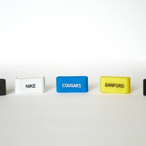 Puede incluir: Cinco llaveros rectangulares de diferentes colores con texto blanco. Los llaveros est&aacute;n etiquetados como "Groms", "Nike", "Cougar", "Sanford" y "Ditto".