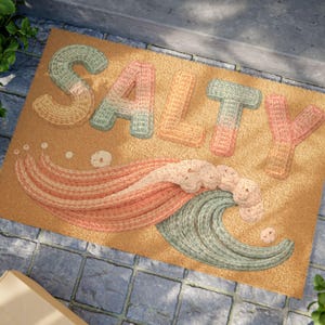 Könnte beinhalten: Eine rechteckige Fußmatte mit dem Wort "SALTY" in großen, strukturierten Buchstaben. Die Buchstaben sind in Grün-, Orange- und Rosatönen gehalten. Darunter befindet sich ein stilisiertes Wellen- und Schnurrbart-Design in ähnlichen Farben.